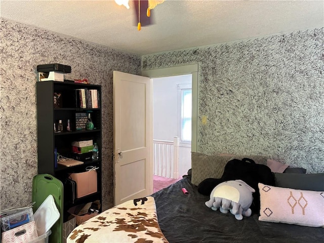 bedroom with wallpapered walls, ceiling fan, and a textured ceiling