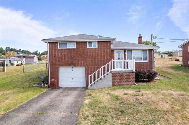 tri-level home featuring driveway, a chimney, an attached garage, a front lawn, and brick siding