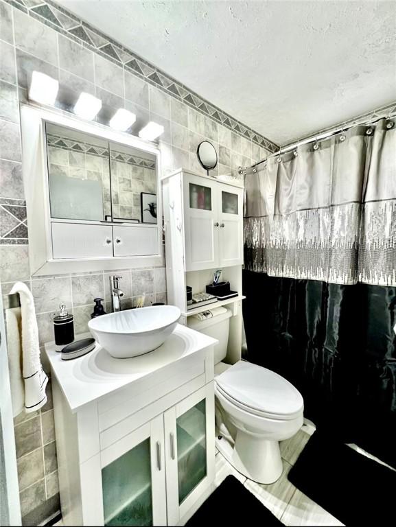 full bathroom with tile walls, toilet, vanity, curtained shower, and backsplash