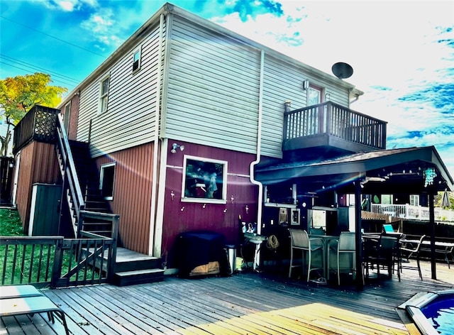 rear view of house with a balcony, outdoor dining space, stairs, and a wooden deck