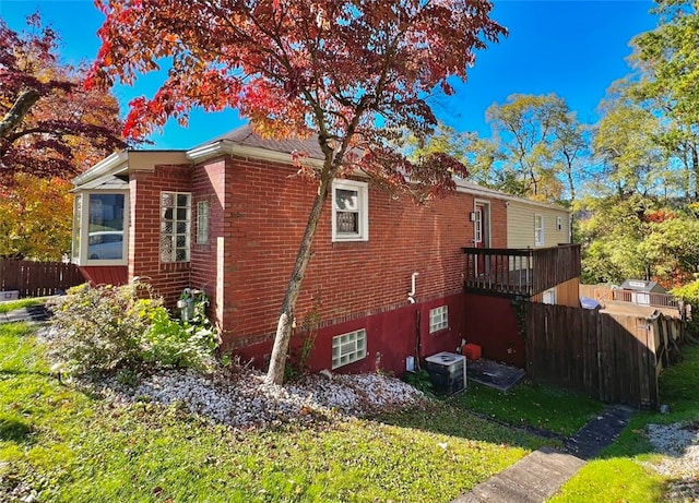 view of side of property featuring a yard, brick siding, fence, and central air condition unit