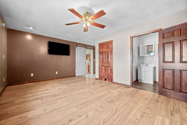 unfurnished bedroom featuring a barn door, ceiling fan, connected bathroom, and light hardwood / wood-style floors