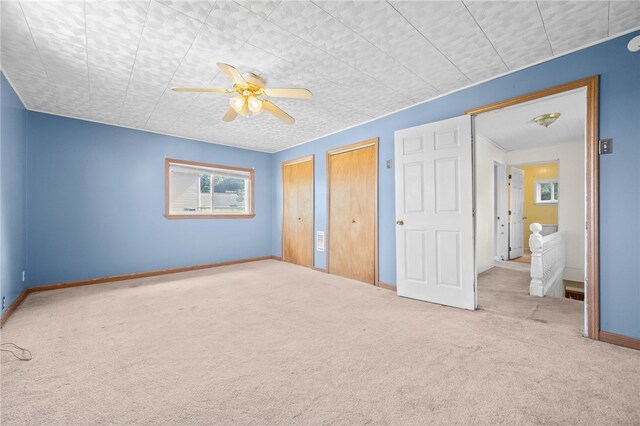 unfurnished bedroom with ceiling fan, light carpet, and two closets