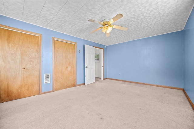 unfurnished bedroom with ceiling fan, carpet floors, and multiple closets