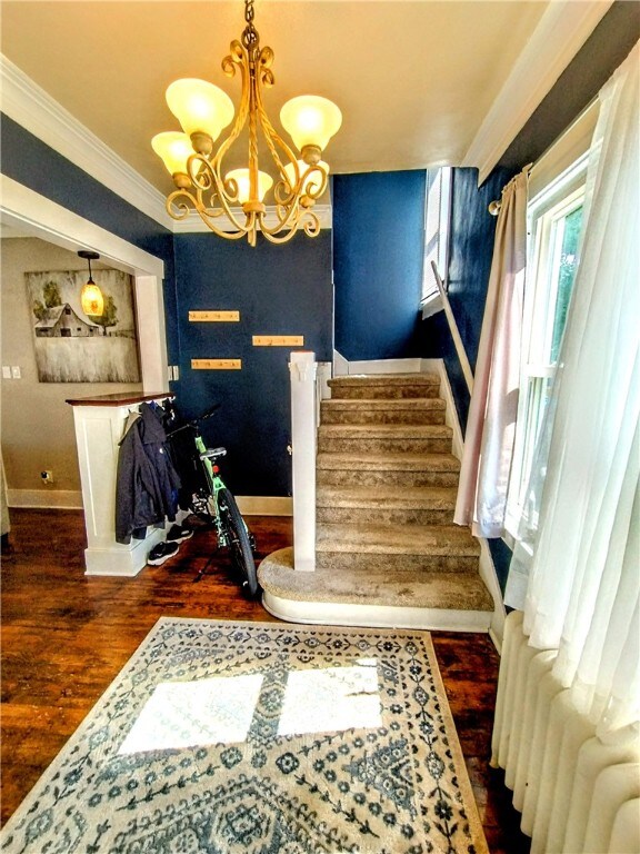 staircase featuring hardwood / wood-style flooring, crown molding, and a notable chandelier