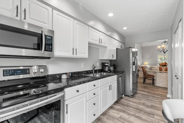 kitchen featuring white cabinetry, sink, light hardwood / wood-style flooring, a notable chandelier, and appliances with stainless steel finishes