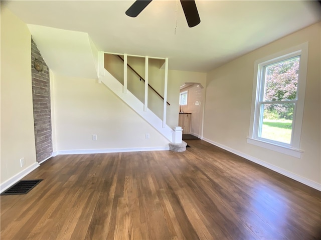 unfurnished living room featuring ceiling fan, wood-type flooring, and brick wall