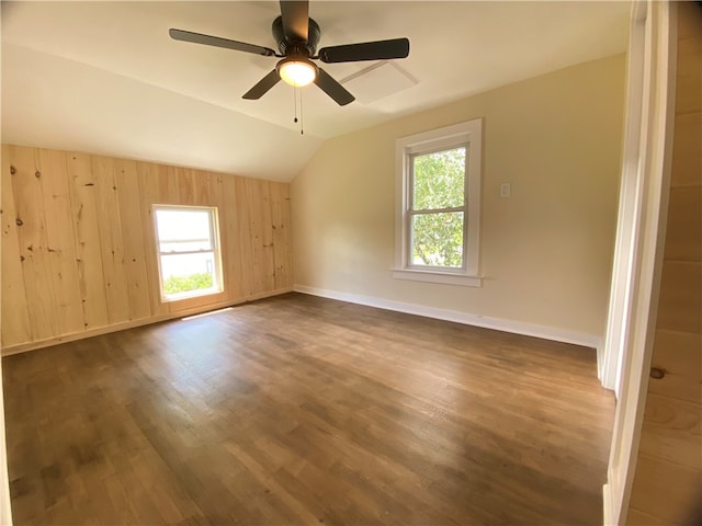 empty room featuring ceiling fan, dark hardwood / wood-style floors, wood walls, and lofted ceiling