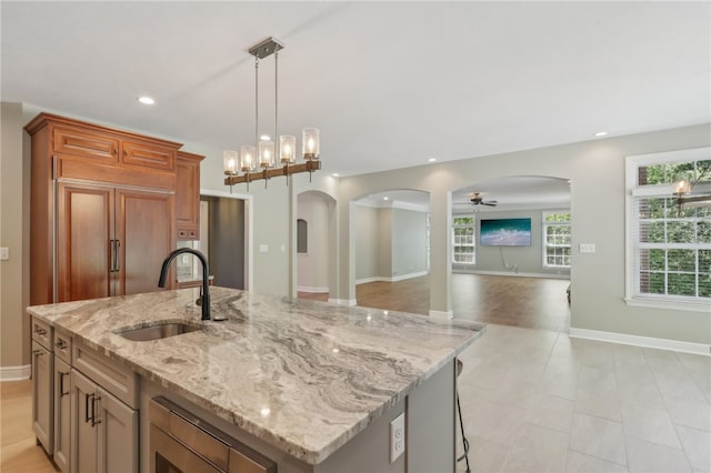 kitchen featuring ceiling fan, sink, light stone countertops, an island with sink, and decorative light fixtures