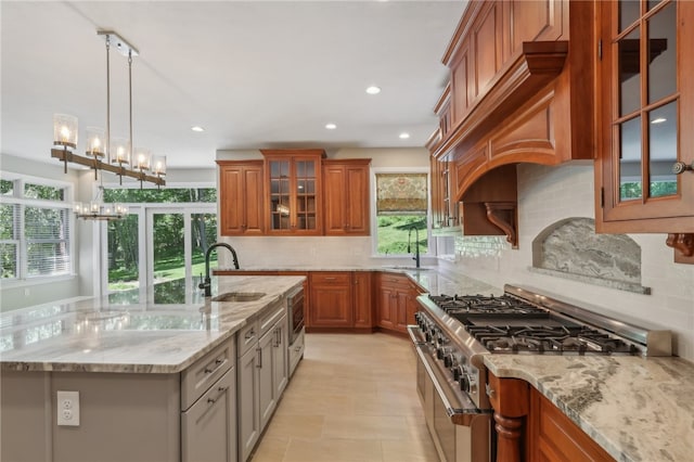 kitchen with light stone countertops, tasteful backsplash, high end stove, sink, and a chandelier