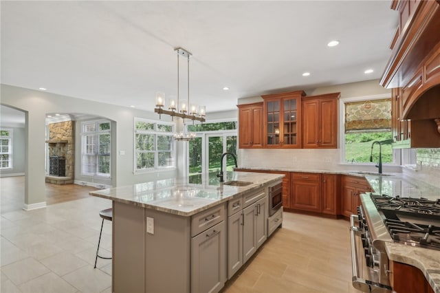 kitchen featuring light stone countertops, backsplash, stainless steel appliances, a kitchen island with sink, and a chandelier