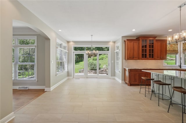 kitchen with decorative backsplash, light stone counters, decorative light fixtures, a notable chandelier, and a breakfast bar area