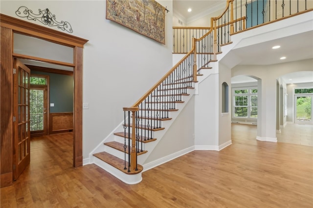 stairs with crown molding, wood-type flooring, and a high ceiling