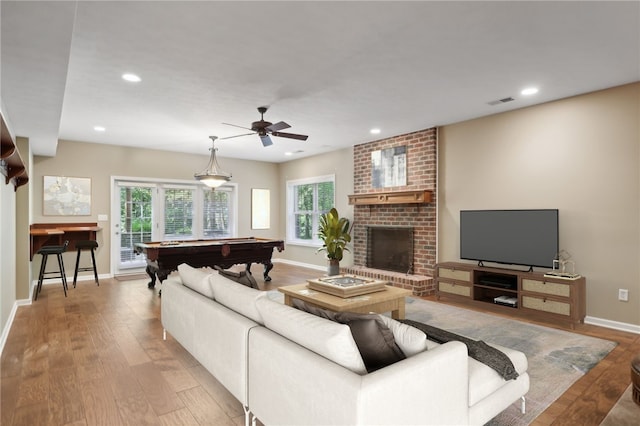 living room featuring light wood-type flooring, a brick fireplace, ceiling fan, and pool table