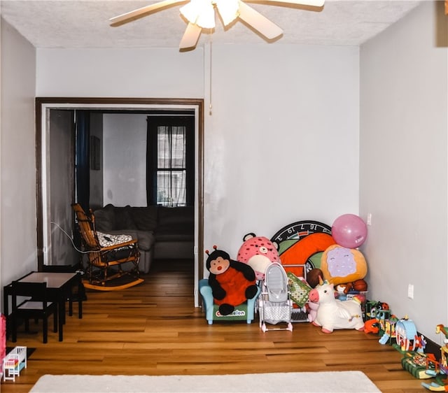 recreation room with a textured ceiling, ceiling fan, and hardwood / wood-style flooring