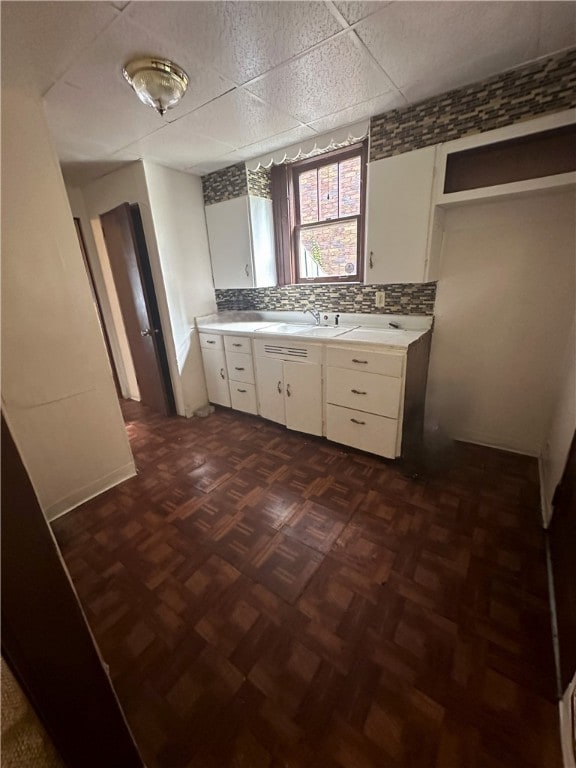 kitchen featuring sink, a drop ceiling, decorative backsplash, dark parquet floors, and white cabinets