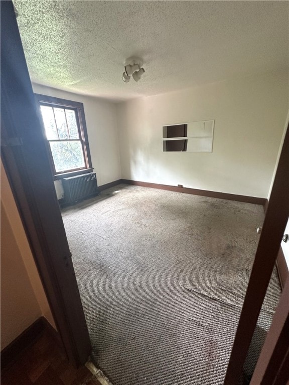 spare room with a textured ceiling, carpet floors, and radiator