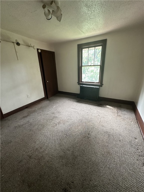 carpeted empty room featuring a textured ceiling and radiator heating unit