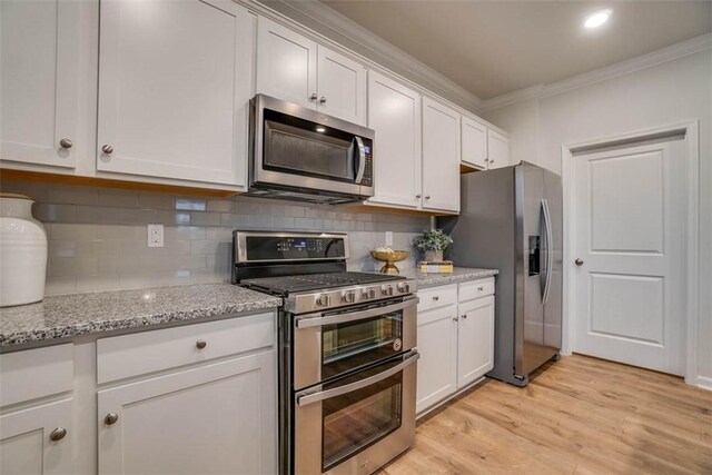 kitchen featuring light stone counters, white cabinetry, appliances with stainless steel finishes, crown molding, and light hardwood / wood-style floors