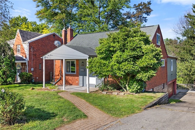 view of front facade featuring brick siding, a chimney, a front yard, and roof with shingles