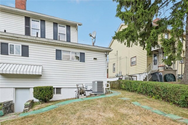 back of house with central air condition unit and a yard