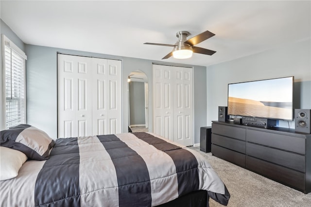 bedroom featuring ceiling fan, light carpet, and multiple closets