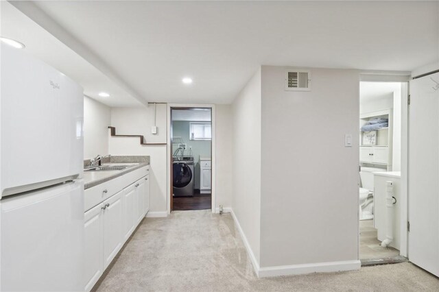 kitchen featuring washer / clothes dryer, white cabinetry, light colored carpet, and white refrigerator