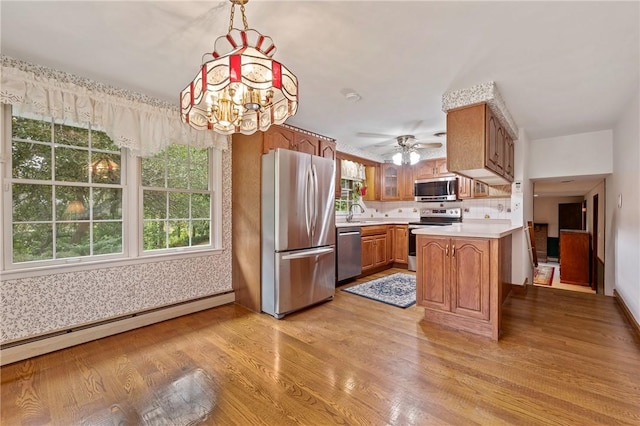 kitchen featuring stainless steel appliances, a baseboard radiator, light hardwood / wood-style flooring, kitchen peninsula, and pendant lighting