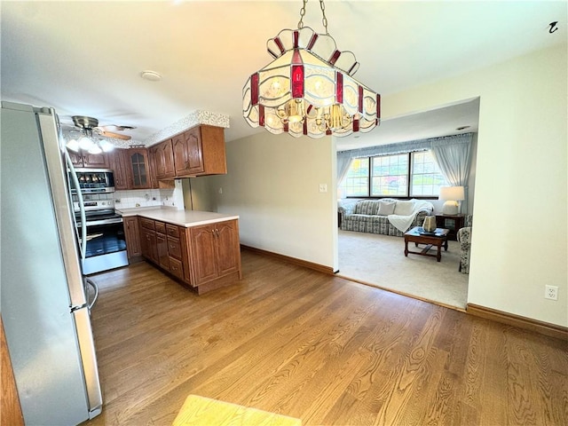 kitchen featuring ceiling fan with notable chandelier, decorative backsplash, light hardwood / wood-style floors, kitchen peninsula, and stainless steel appliances