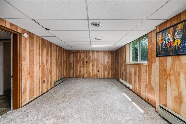 unfurnished room with carpet, wood walls, a paneled ceiling, and a baseboard radiator