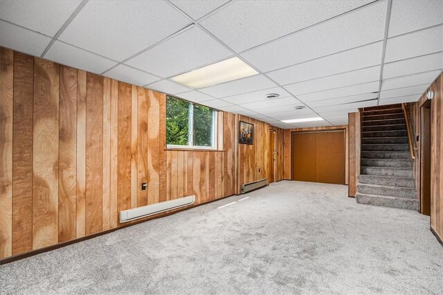 basement featuring a baseboard radiator, wood walls, a paneled ceiling, and carpet flooring