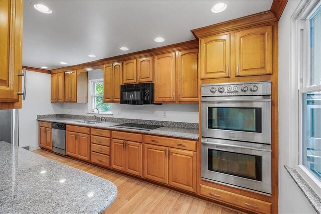 kitchen featuring sink, light stone counters, black appliances, and light wood-type flooring