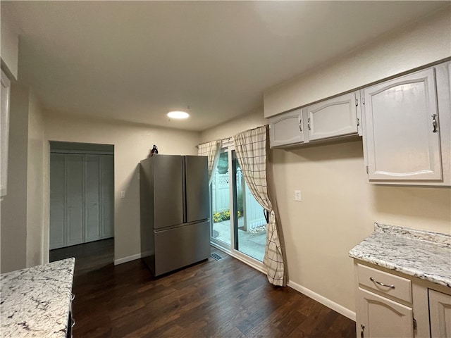 kitchen featuring light stone countertops, dark hardwood / wood-style floors, stainless steel refrigerator, and white cabinetry