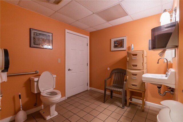 bathroom featuring toilet, sink, a paneled ceiling, and tile patterned floors