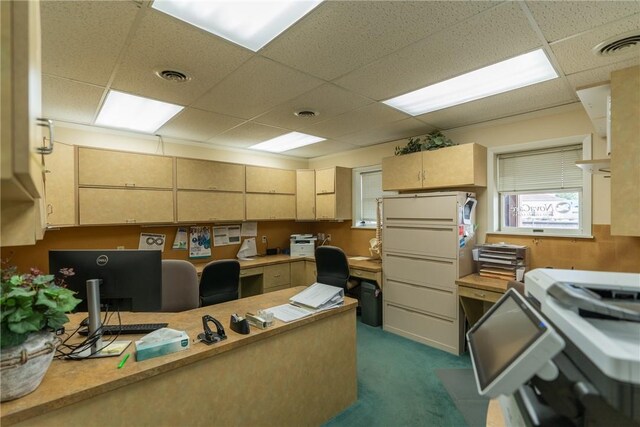 interior space with dark carpet, built in desk, light brown cabinets, and a drop ceiling