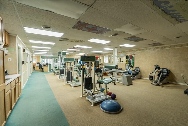 gym with a paneled ceiling and light colored carpet