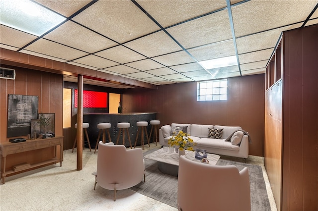 carpeted living room with a paneled ceiling, bar, and wooden walls