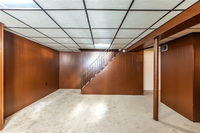 basement featuring wood walls, a drop ceiling, and carpet floors