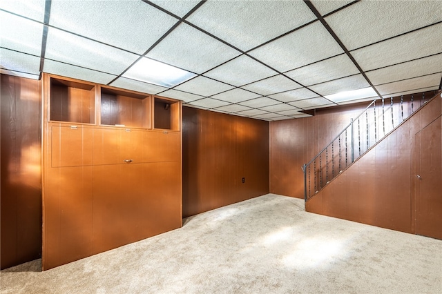 basement featuring carpet flooring, wood walls, and a drop ceiling