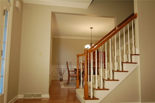 stairs featuring wood-type flooring, a notable chandelier, and ornamental molding