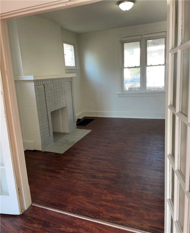 unfurnished living room featuring a fireplace, a healthy amount of sunlight, and dark hardwood / wood-style floors