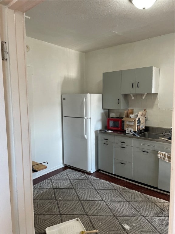 kitchen with white refrigerator, tasteful backsplash, dark tile patterned floors, and sink