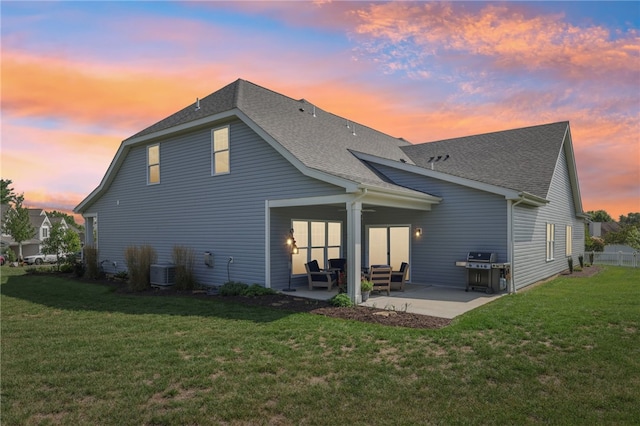 back house at dusk featuring a lawn, a patio area, and central air condition unit