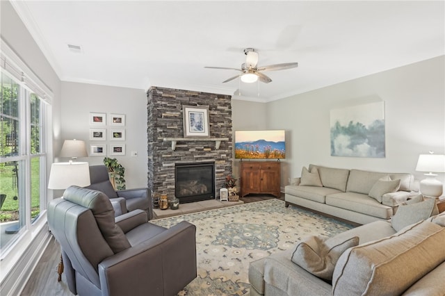 living room featuring a healthy amount of sunlight, ceiling fan, a stone fireplace, and light wood-type flooring