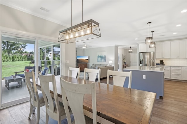 dining room featuring ceiling fan with notable chandelier, light wood-type flooring, crown molding, and sink