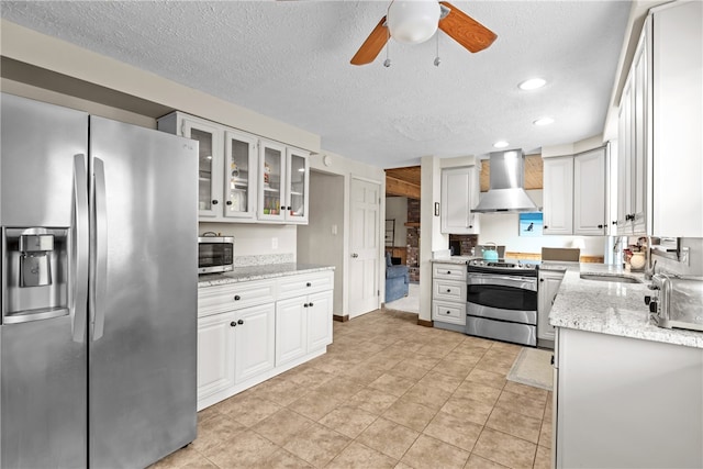 kitchen with white cabinets, stainless steel appliances, sink, wall chimney range hood, and ceiling fan