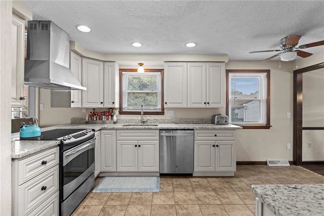 kitchen featuring stainless steel appliances, sink, white cabinetry, wall chimney range hood, and light tile patterned flooring