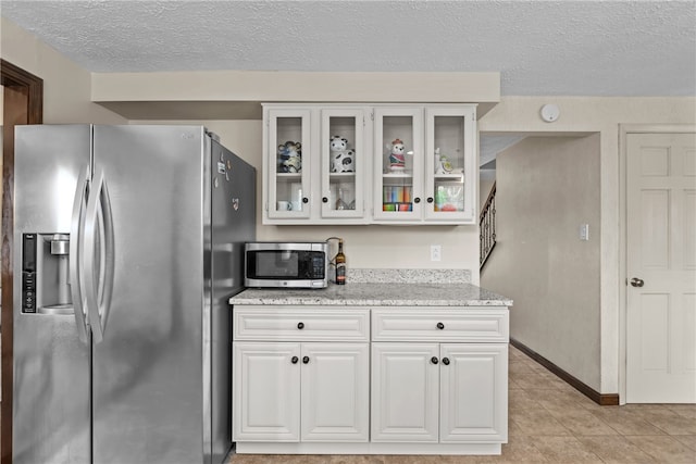 kitchen with appliances with stainless steel finishes, light stone countertops, white cabinetry, light tile patterned flooring, and a textured ceiling