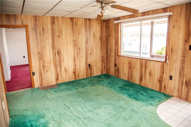 empty room featuring wood walls, ceiling fan, carpet, and a drop ceiling