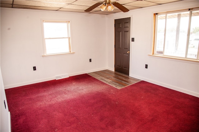 carpeted spare room with ceiling fan and a drop ceiling